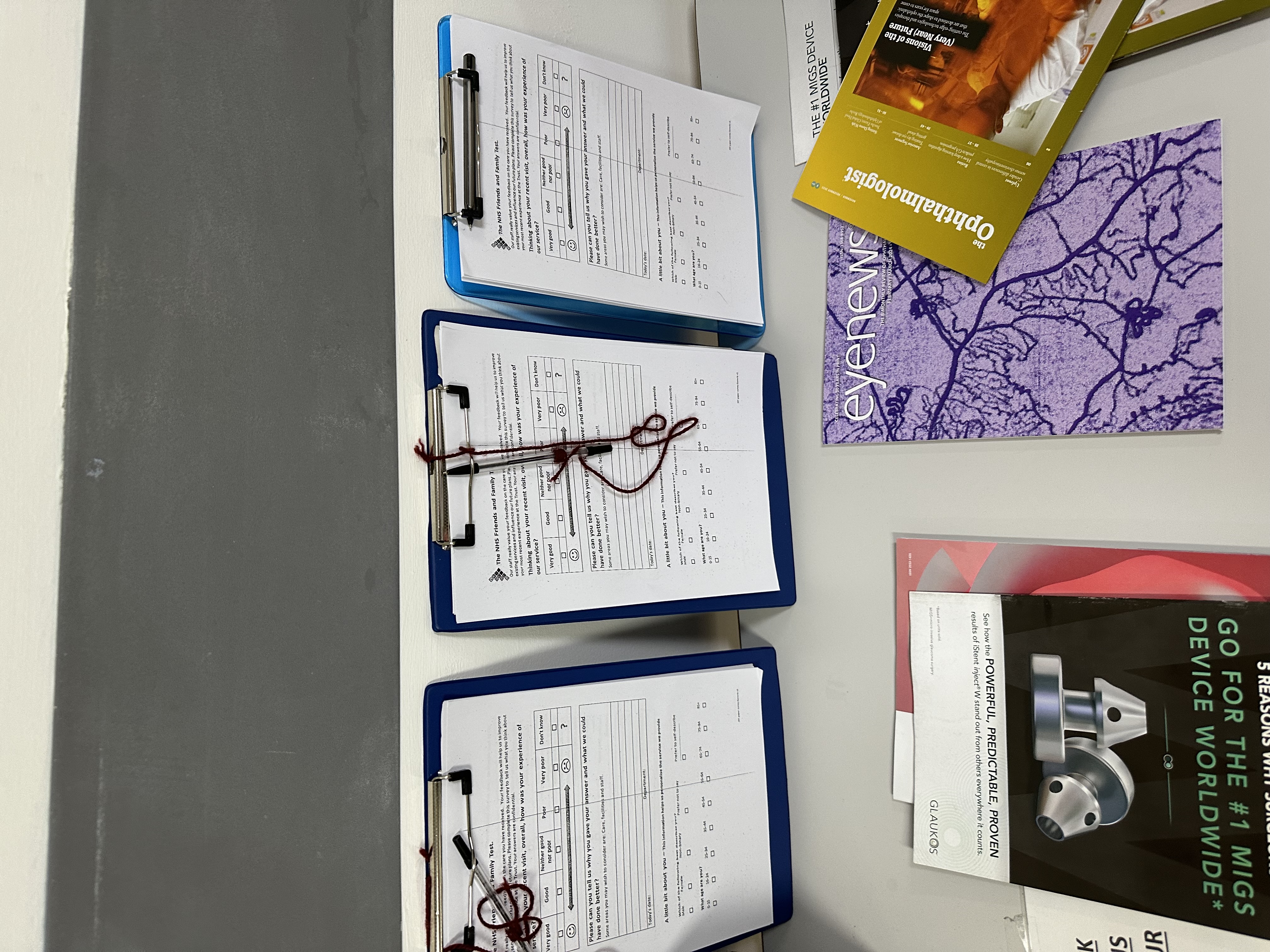 A table at the eye clinic at Chelsea and Westminster Hospital which has leaflets containing health information and clipboards with feedback forms that patient can fill in.