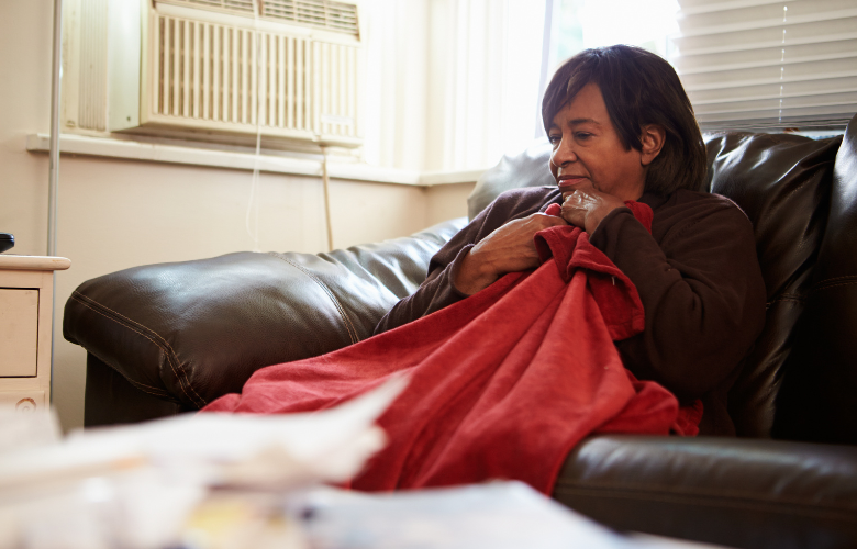 An middle-aged woman with a blanket on her lap as she sits on the sofa to keep warm.