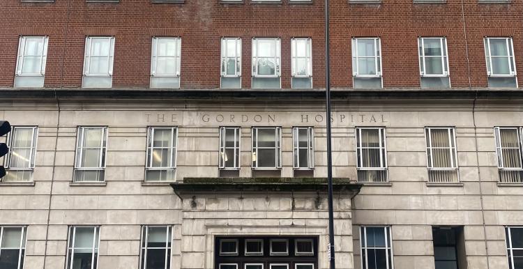 a photo of the entrance of the Gordon Hospital, a woman is walking nearby