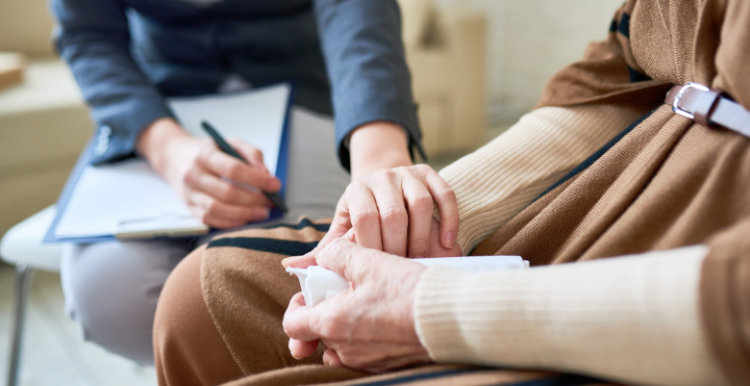 A doctor holding a pen, with a clipboard on their lap, and comforting a patient