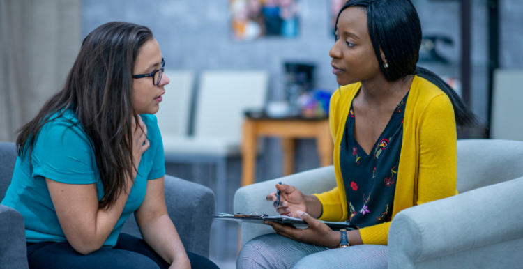 Two women talking to eachother. The woman on the right is taking notes of what's being said.