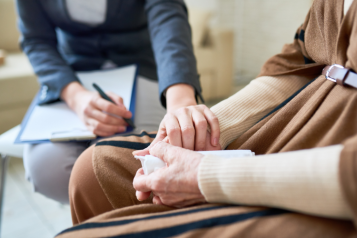 A doctor holding a pen, with a clipboard on their lap, and comforting a patient