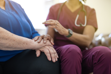 A hospice nurse in a purple uniform comforting an elderly person.